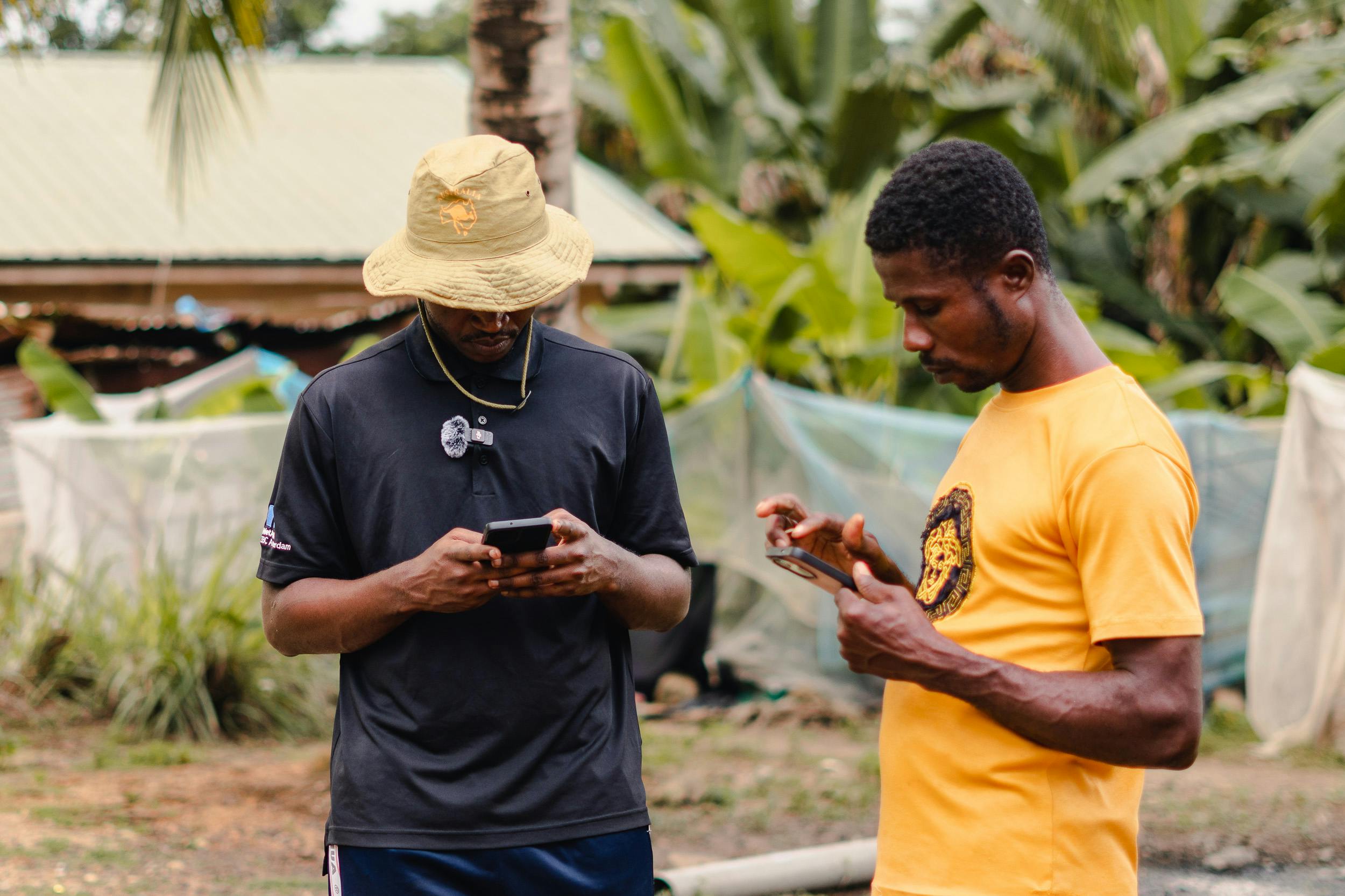 Two adult men focused on their smartphones while outdoors surrounded by greenery.